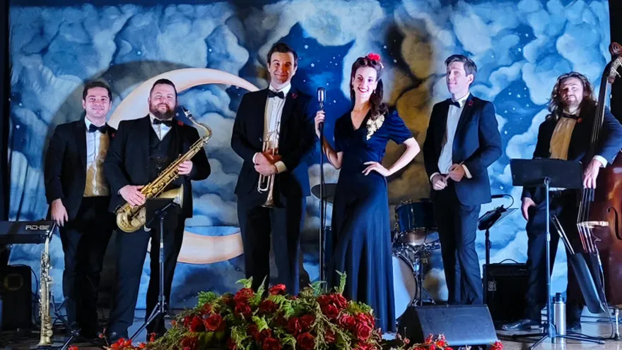 Ashley Anne in a navy velvet gown with the full Carnations ensemble in black tie before a painted moonlit backdrop