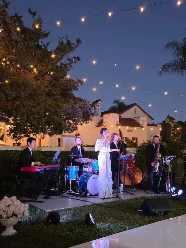 Ashley Anne & The Carnations performing under string lights at dusk at a Spanish-style private estate wedding