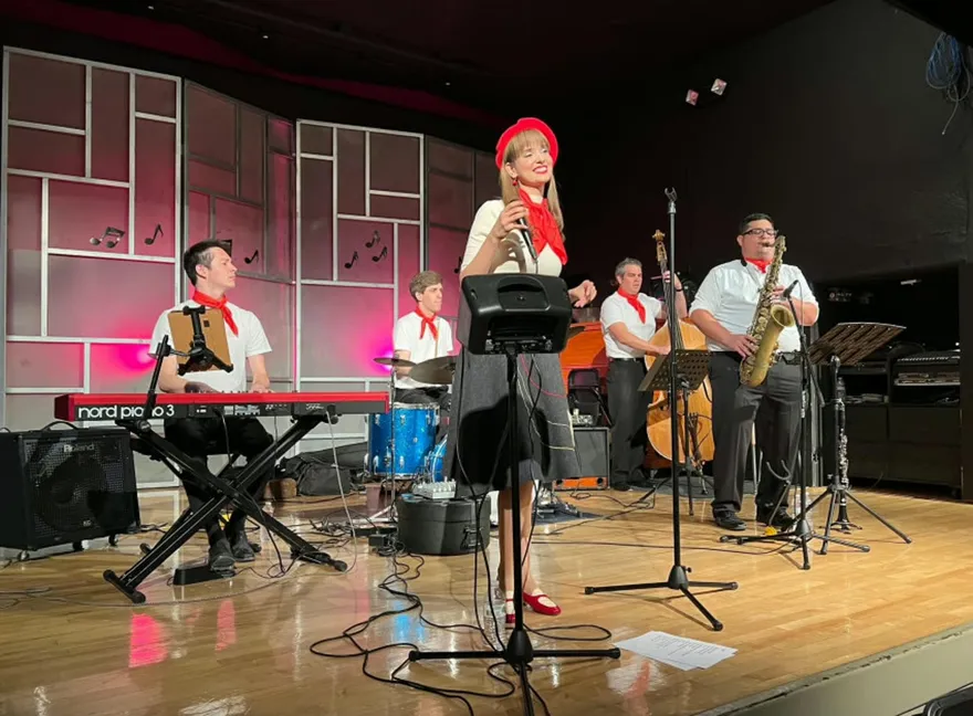 Ashley Anne in a red beret and neckerchief singing with The Carnations dressed in French café style